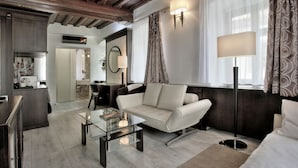 Un salon moderne avec un canapé, une table basse et un lampadaire. On aperçoit un coin cuisine au fond.