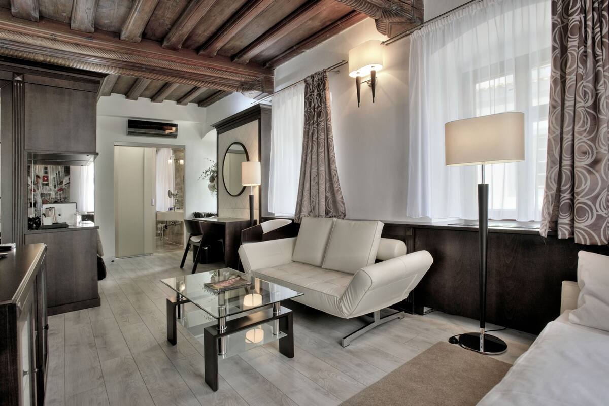 Una sala de estar moderna con un sofá, una mesa de centro y una lámpara de pie. Se observa un área de cocina al fondo.