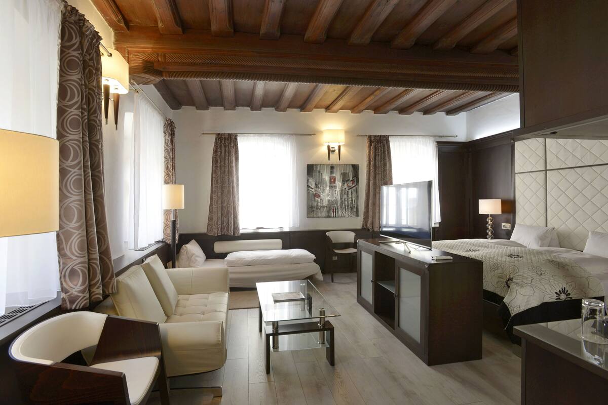 Una habitación de hotel moderna con un sofá, una mesa de centro de vidrio, una cama con colcha y un televisor.