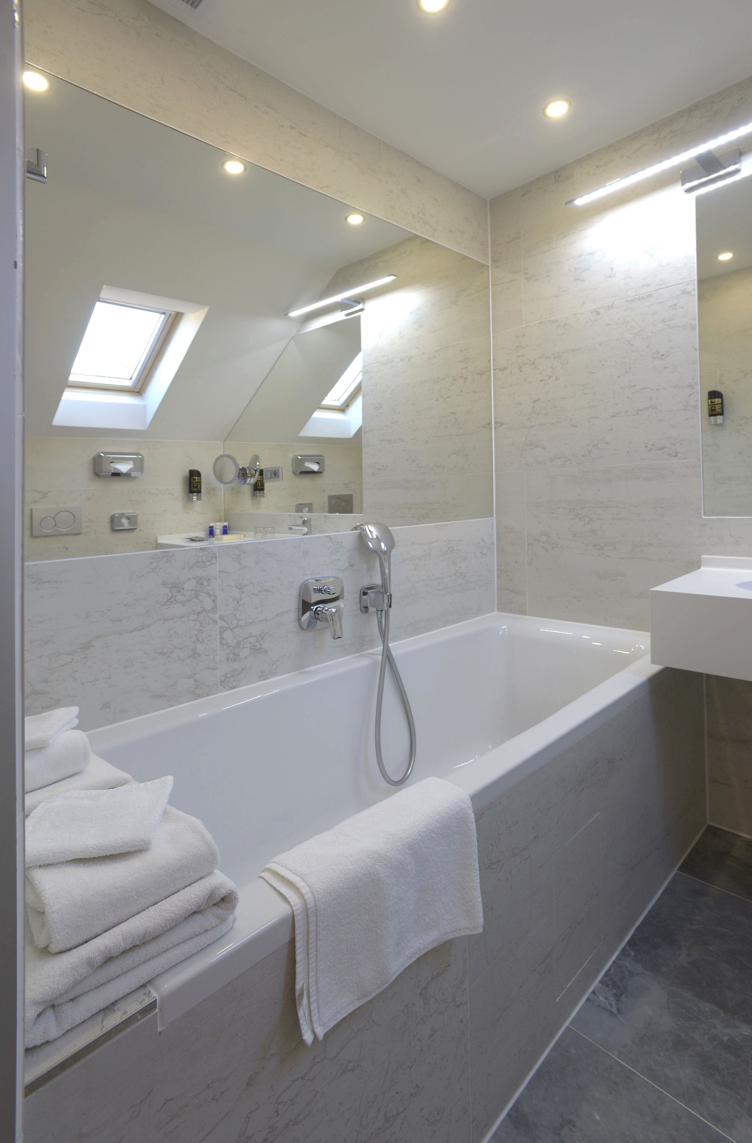 A modern bathroom with a large bathtub, a sink, and a mirror. There are towels stacked on the side of the tub.