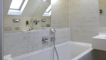 A modern bathroom with a large bathtub, a sink, and a mirror. There are towels stacked on the side of the tub.