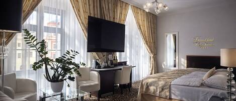 A hotel room with a bed, a desk, a TV, a sofa, and a large window with curtains.