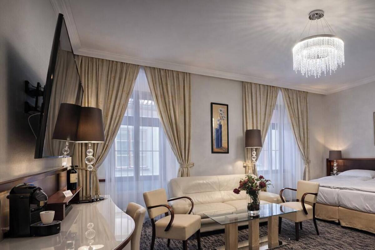 Habitación de hotel con cama, sofá, cafetera, mesa y candelabro.