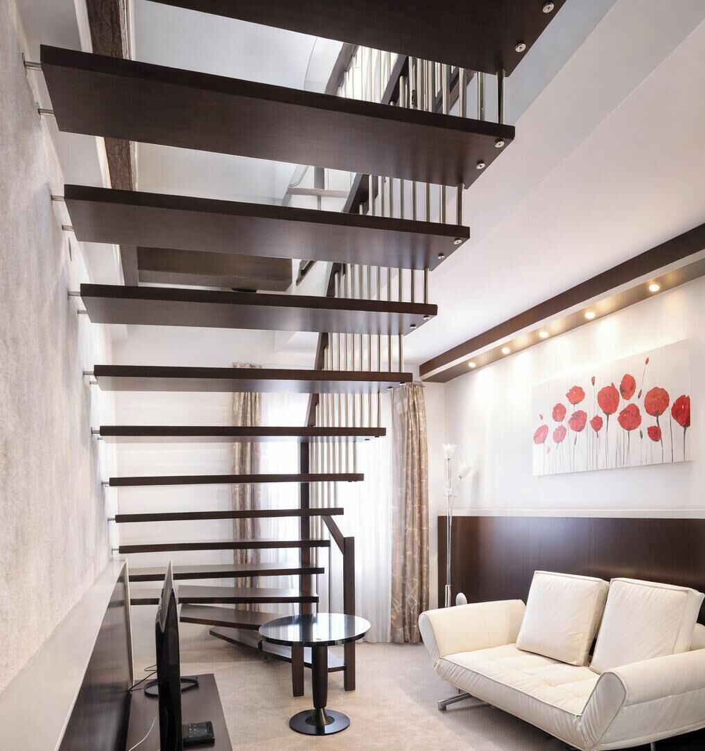 A modern interior with a spiral staircase, a round table, a sofa, and a wall with a floral painting.
