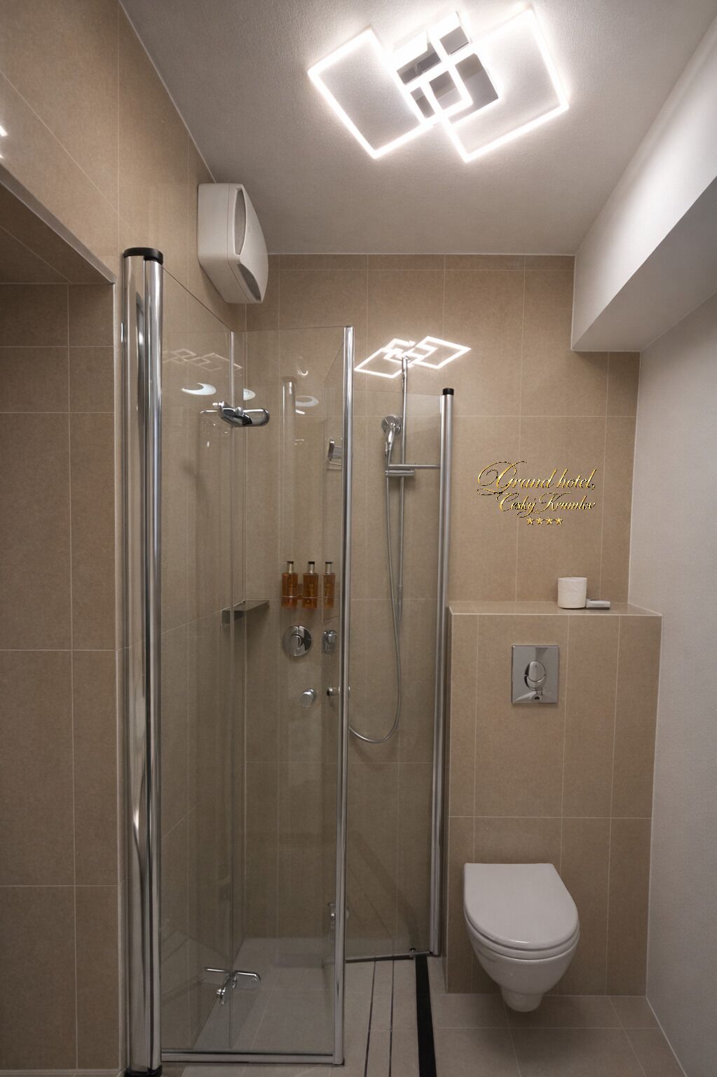 Un bagno moderno con doccia vetrata, un water e un dispenser di sapone fissato alla parete.