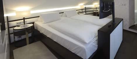 A modern hotel room with a neatly made bed, bedside tables, and a TV on a stand.