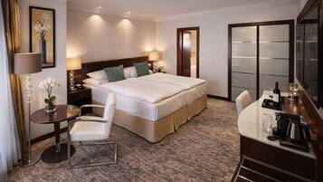 A hotel room with a large bed, a desk with a chair, a vanity with a mirror, and a television.