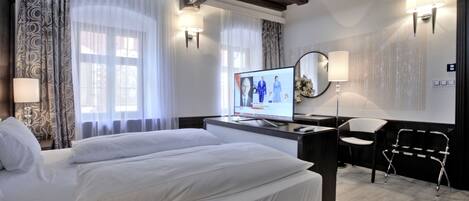 A hotel room with a bed, a desk, a chair, and a television displaying a news program.