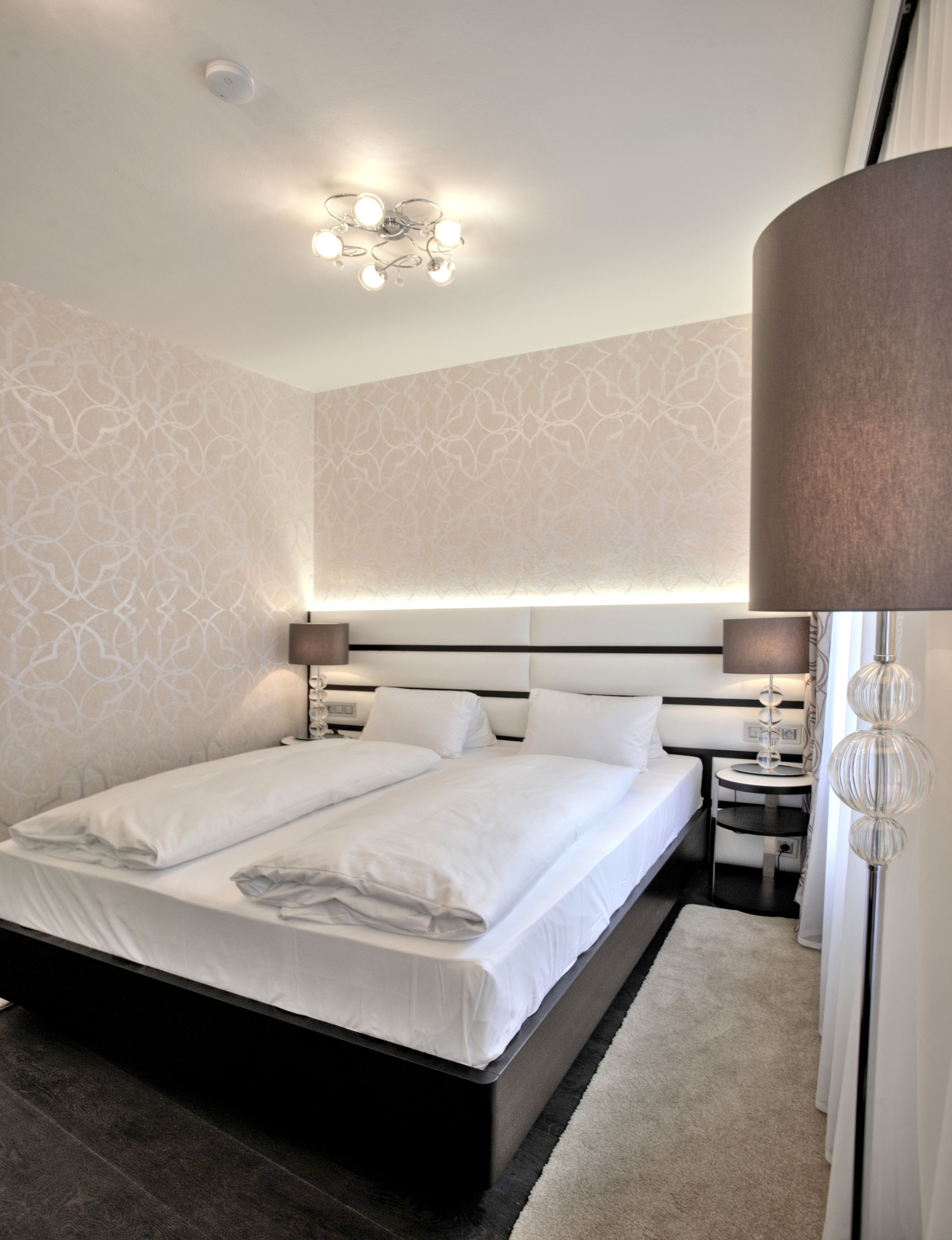 A modern hotel room with a large bed, bedside tables, and a ceiling light fixture.