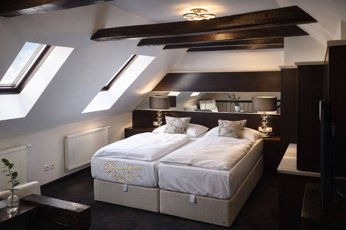 Habitación de hotel con una cama grande, tragaluces, techo oscuro y una mesita de noche con lámpara.