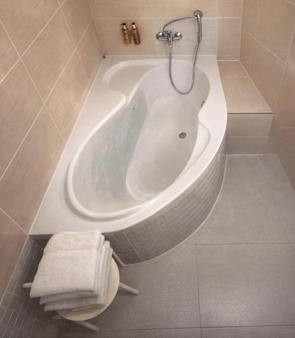 A bathtub with a shower attachment, a stack of white towels, and toiletries on the wall.