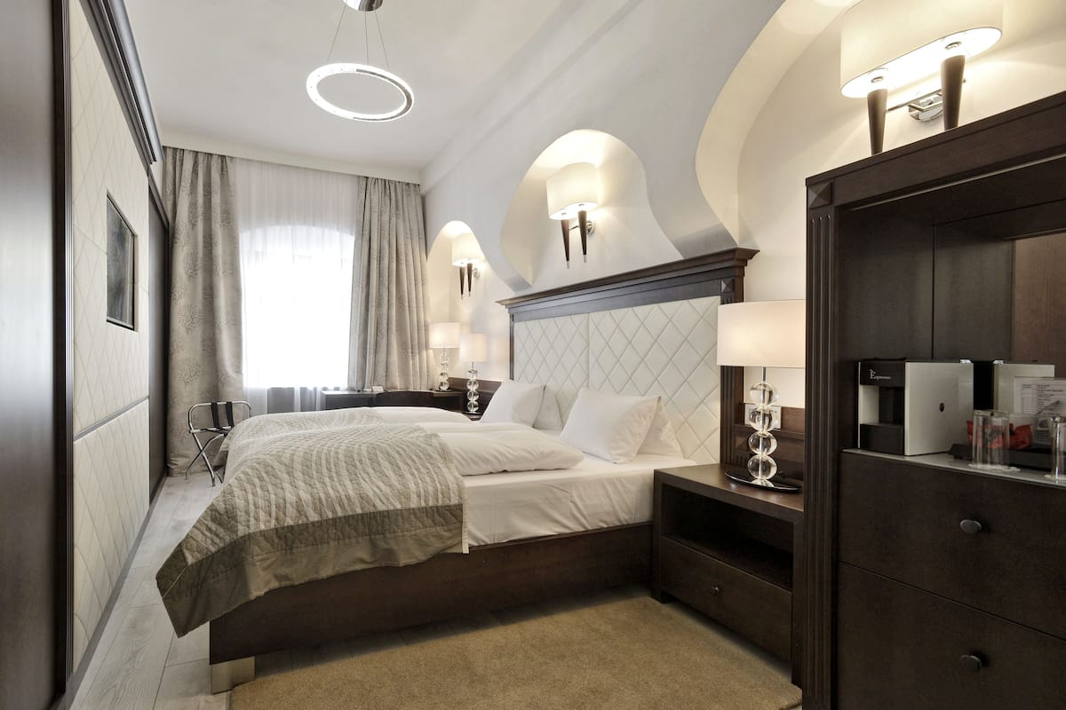 Una habitación de hotel con cama, mesitas de noche, armario y un amplio ventanal con cortinas.