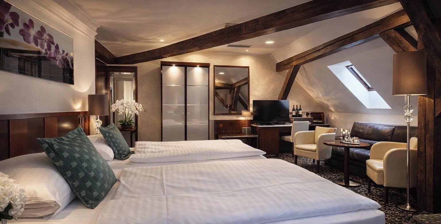 A hotel room with two beds, a desk, a TV, a sofa, and a skylight.