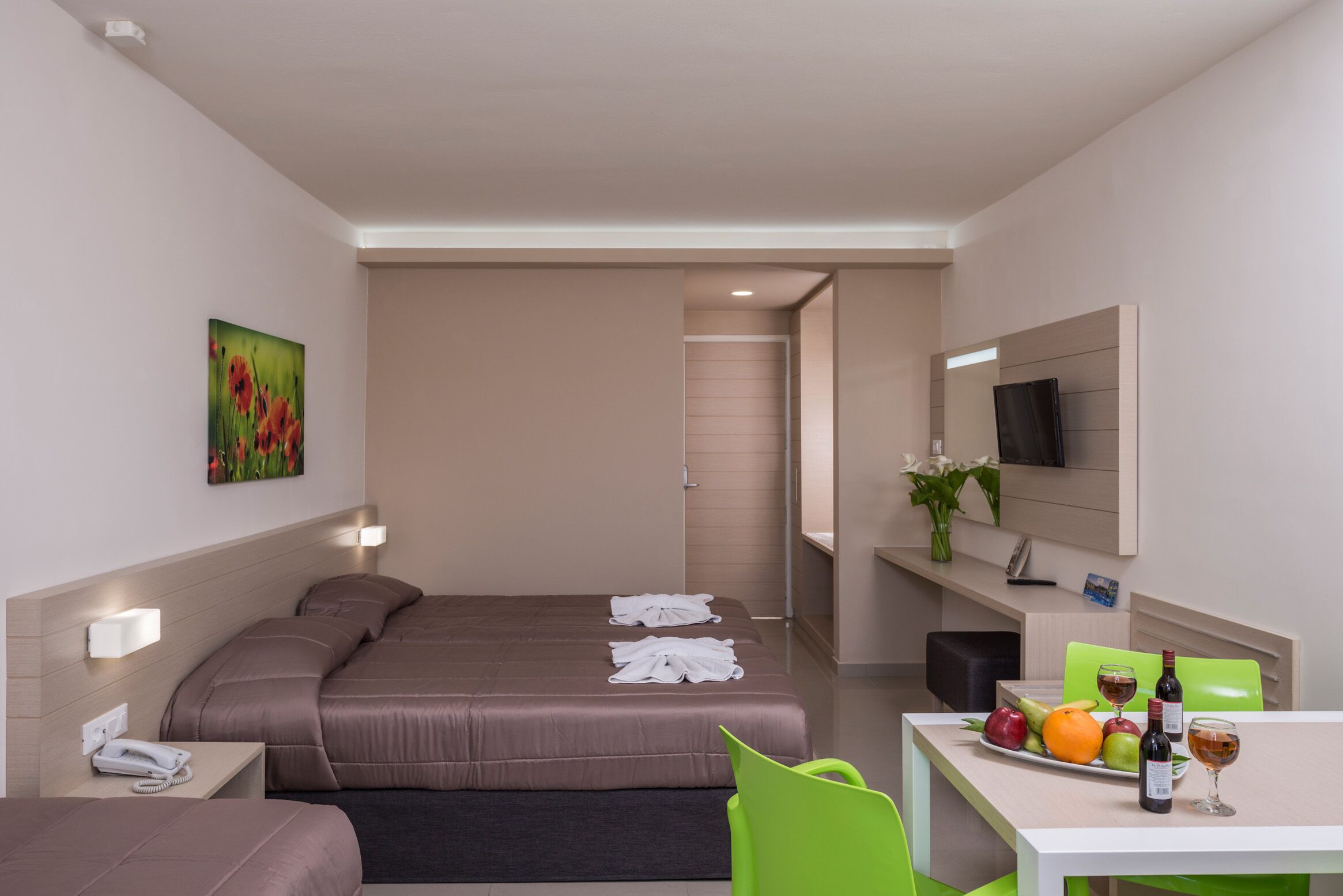 Hotelkamer met een bed, nachtkastje, lamp, televisie en een zithoek met een tafel gedekt voor twee personen.