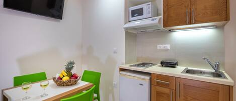 A compact kitchen with a microwave, sink, and a small refrigerator. There is a dining table with chairs and a fruit bowl.