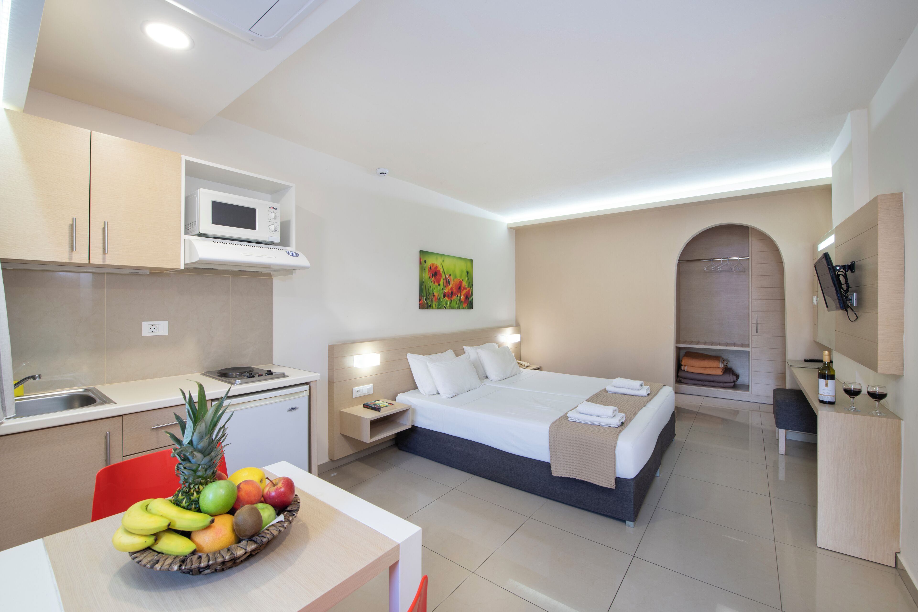 A hotel room with a bed, bedside table, and a small kitchenette.