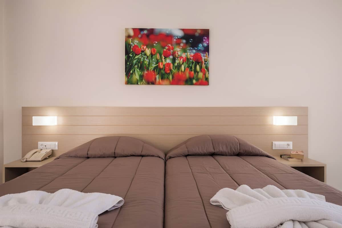 A double bed with brown bedding, two bedside tables, a phone, and a painting of flowers on the wall.