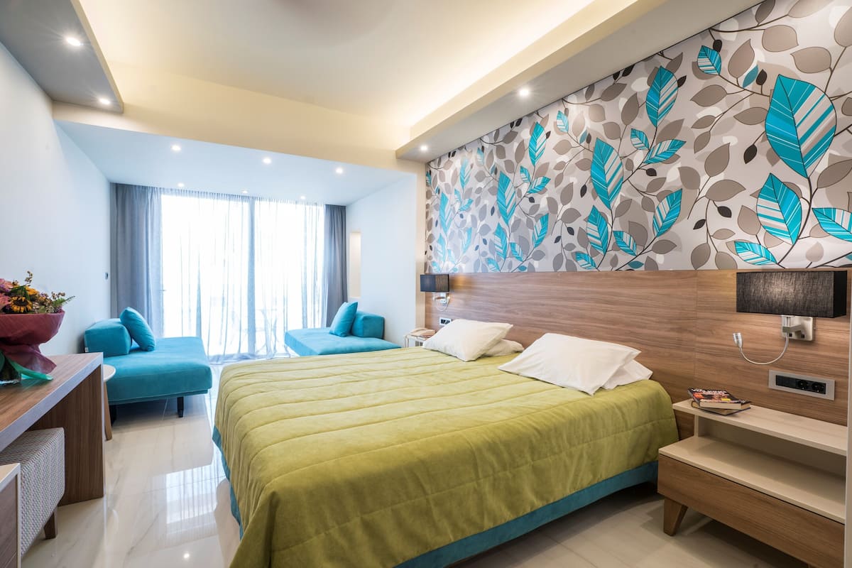 A modern hotel room with a large bed, a desk, a chair, and a sofa.