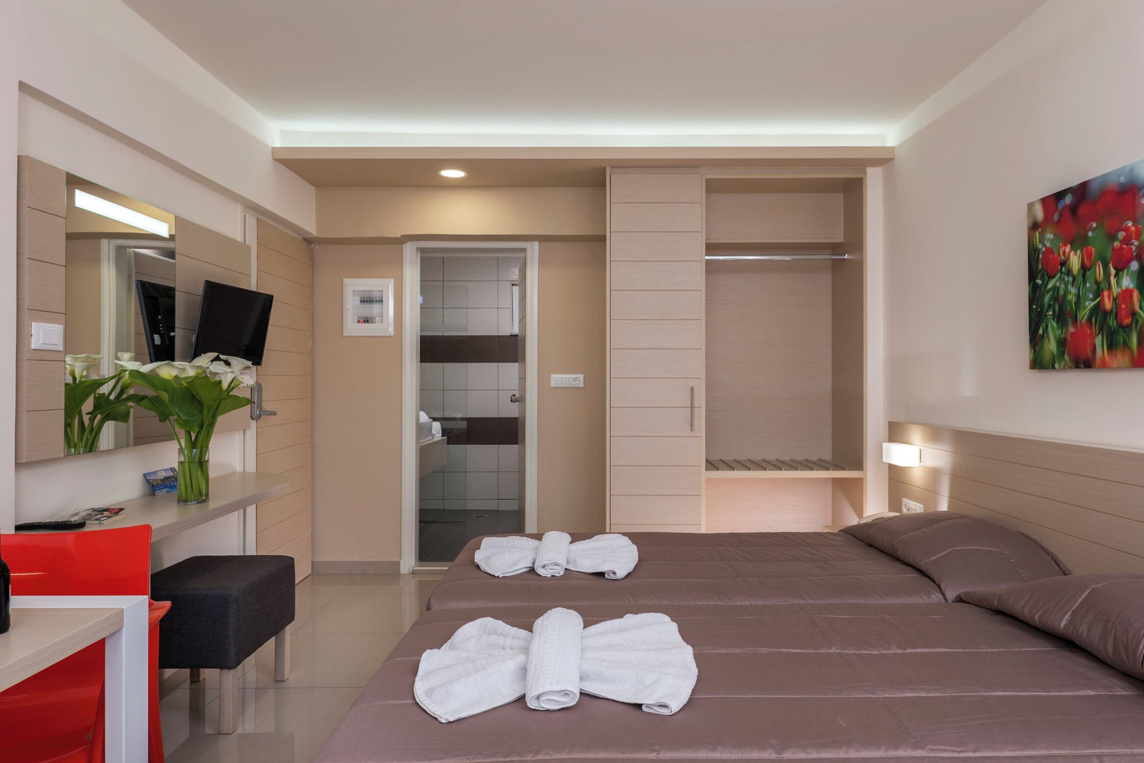 A modern hotel room with a bed, a desk, a chair, a TV, a bathroom, and a closet.