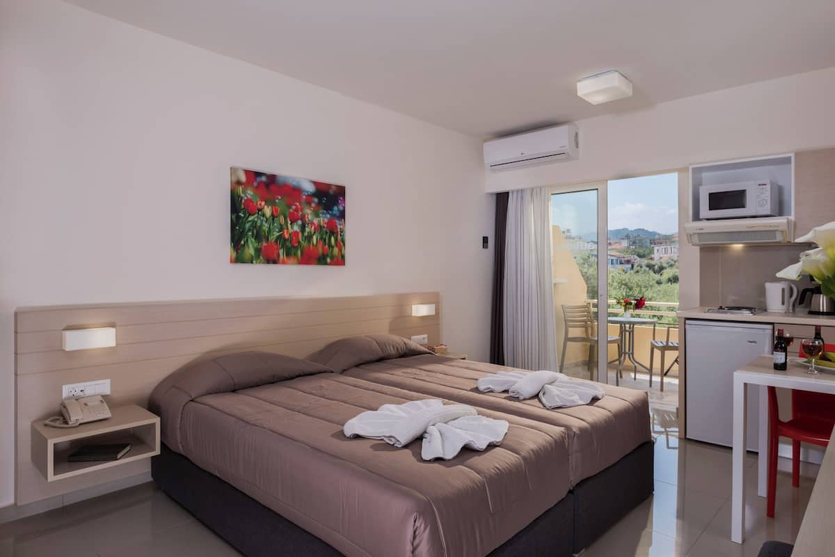 A hotel room with a large bed, a desk with a microwave, and a balcony with a view.