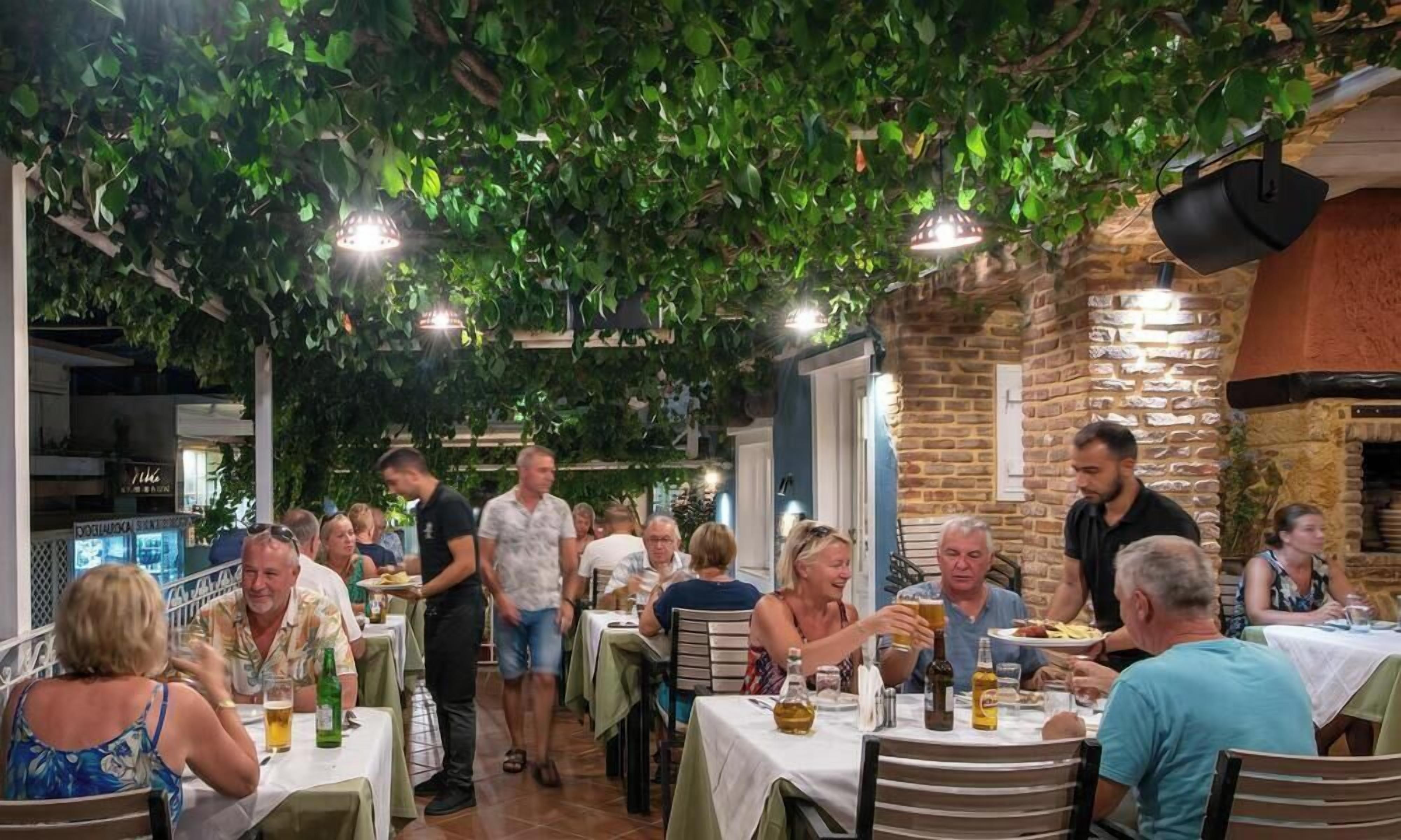 Un espacio de comedor al aire libre con mesas, comensales y un muro de ladrillo.