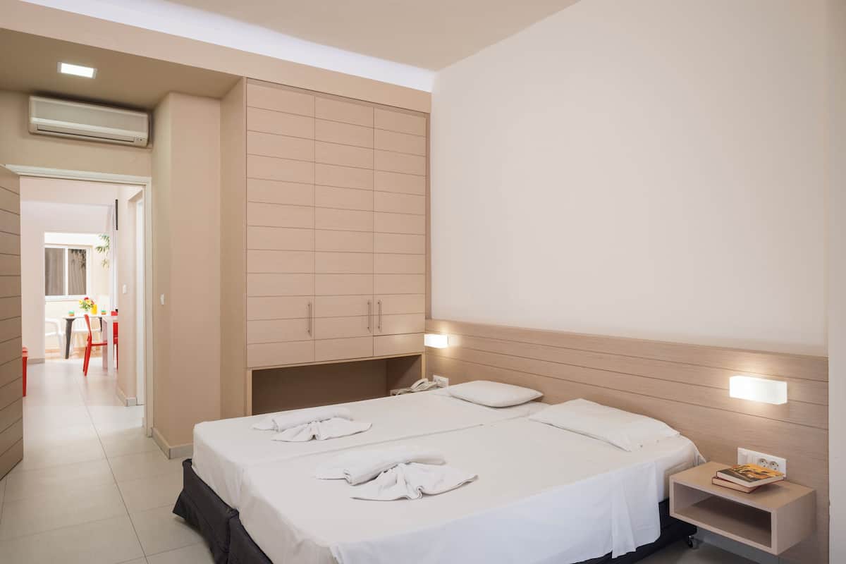 A hotel room with a large bed, a wardrobe, a bedside table with a book, and a bathroom visible through an open door.
