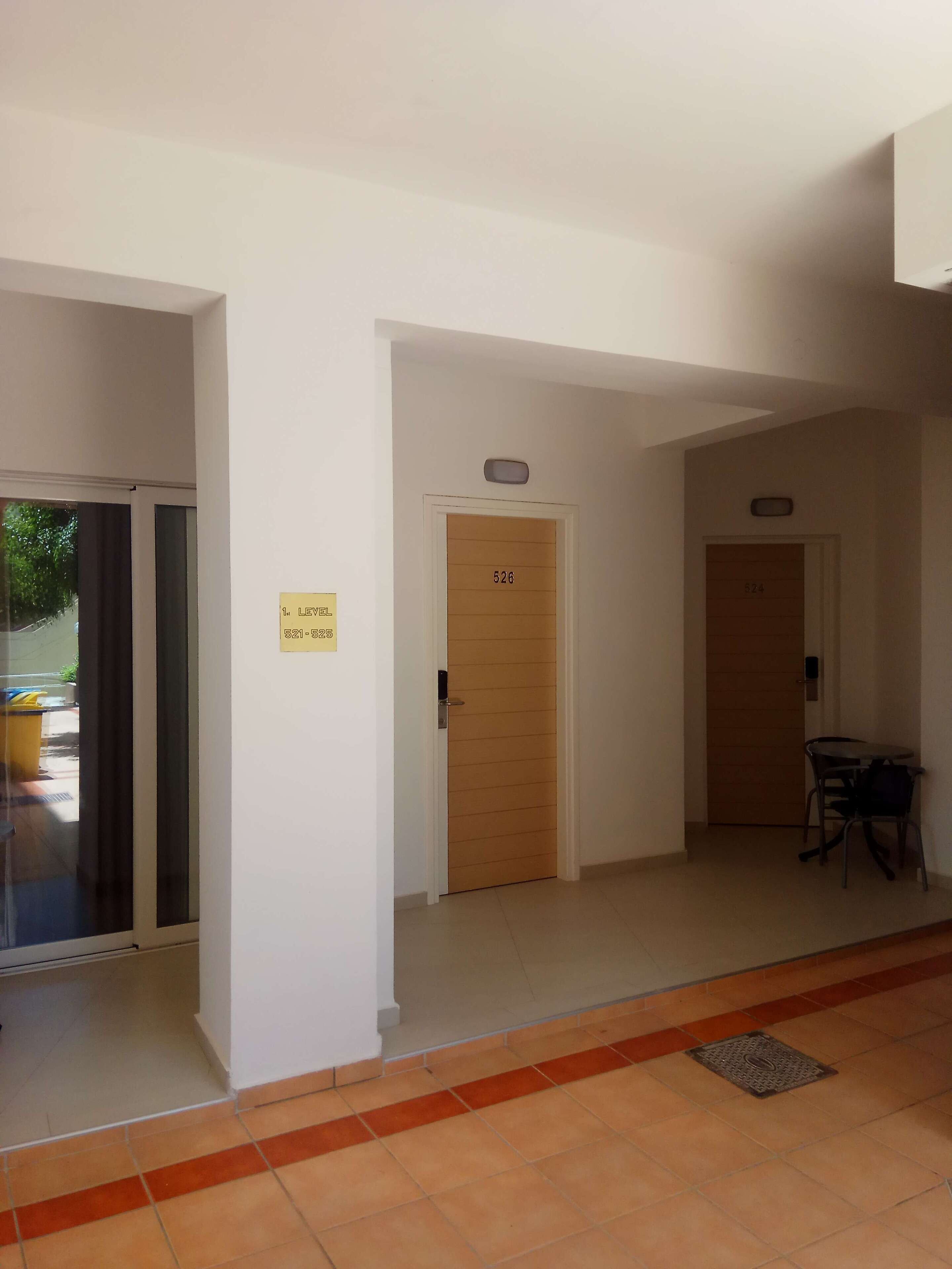 A hallway with doors numbered 526 and 524, a small table with chairs, and a yellow sign on the wall.