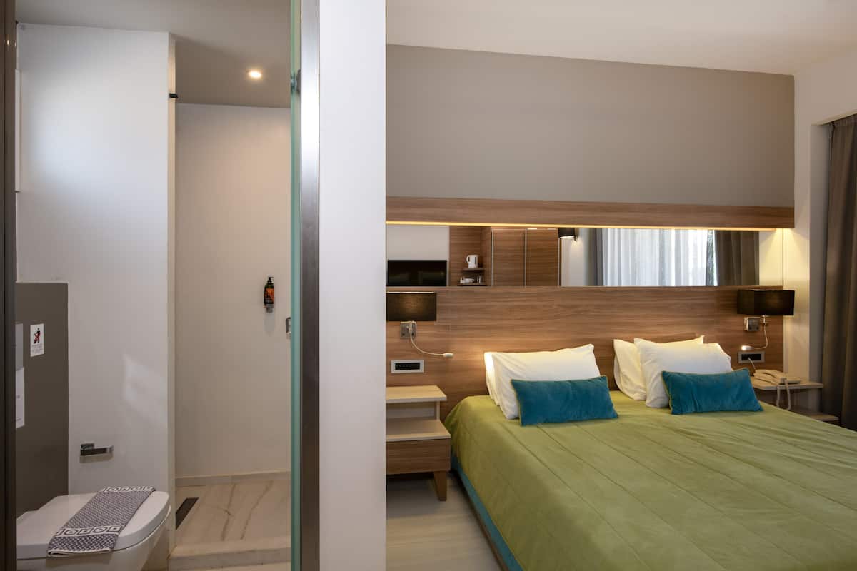 A modern hotel room with a large bed, bedside tables, a mirror, and a shower area.