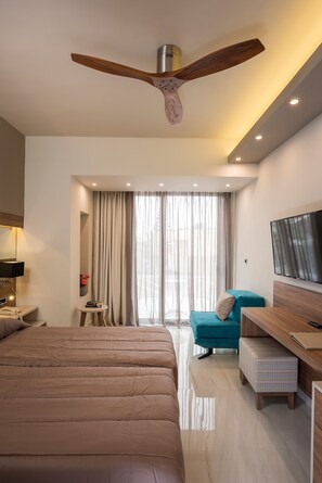A modern hotel room with a large bed, a desk, a TV, and a ceiling fan. - Atrion Hotel (Chania)