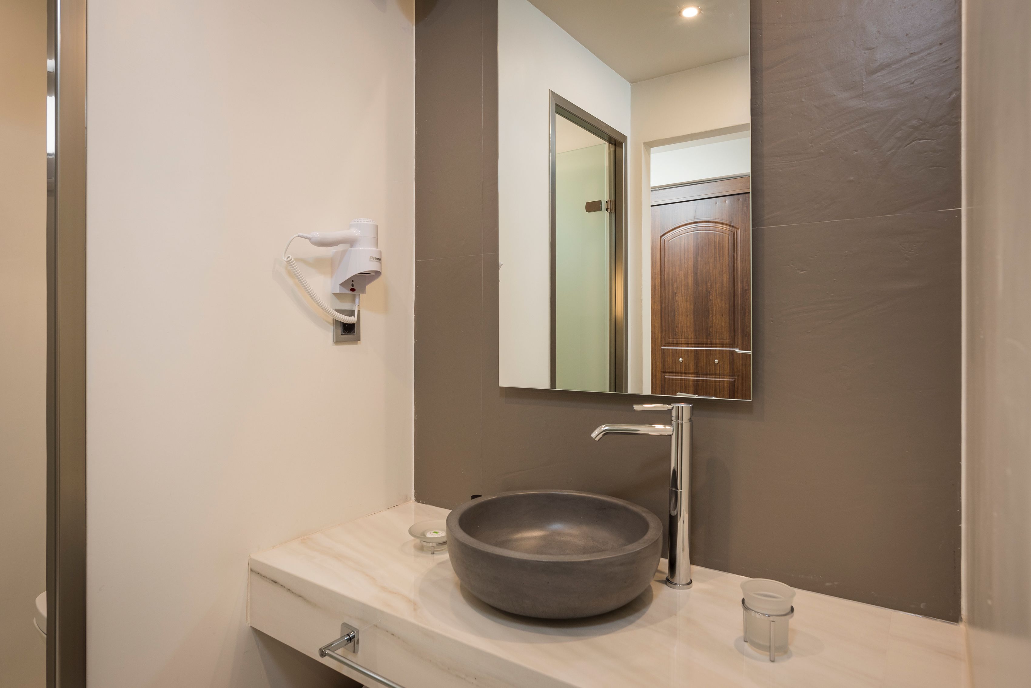 A modern bathroom with a large, round vessel sink, a mirror, a towel dispenser, and a small glass on the counter.