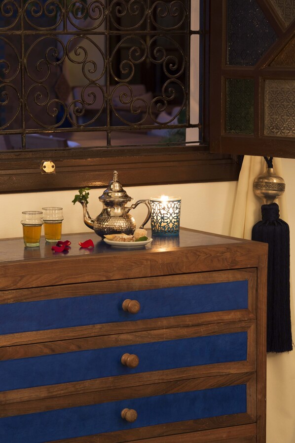 A wooden dresser with blue drawers, a metal teapot, two glasses of beer, and a candle on top.