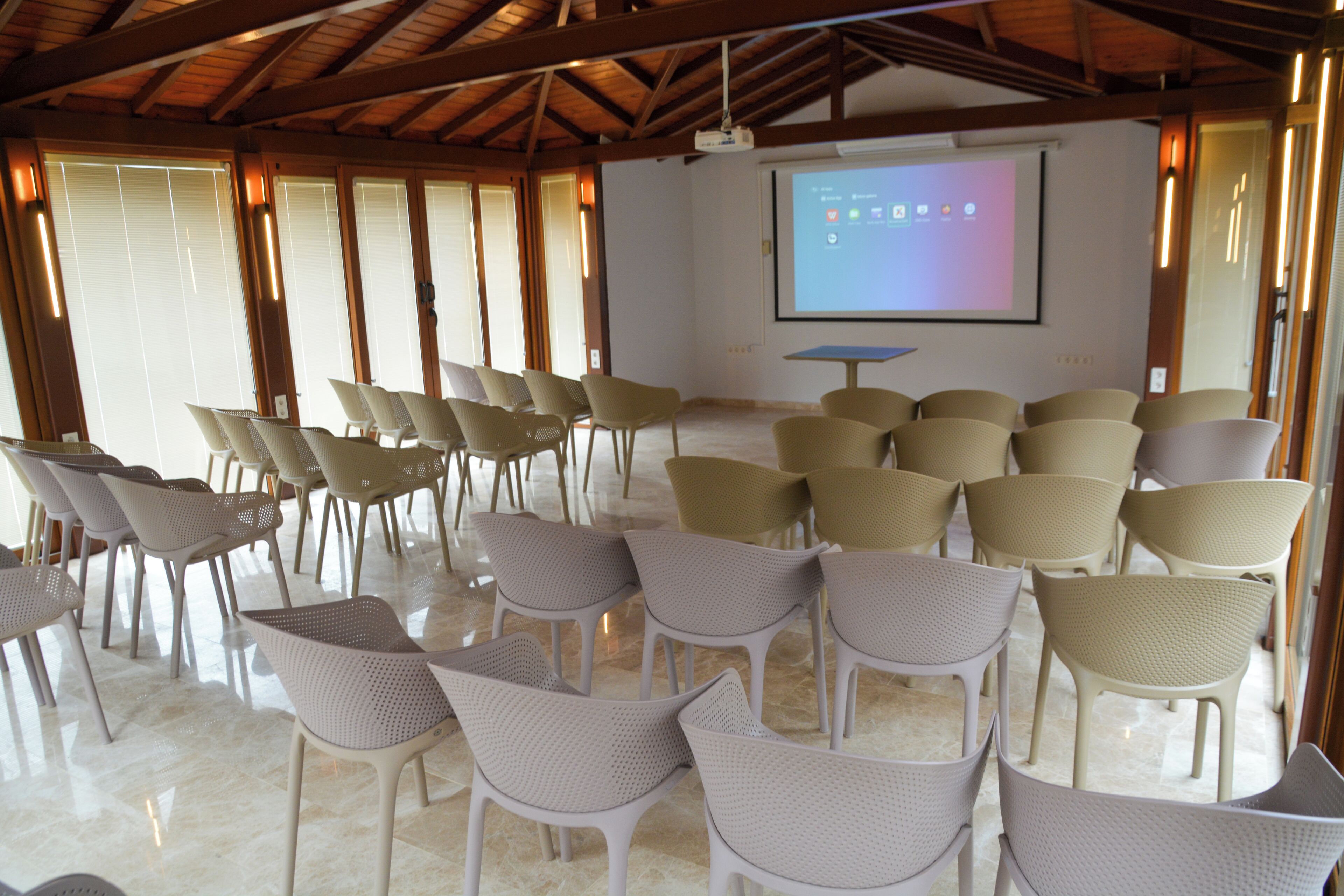 A conference room with rows of chairs, a projector screen, and a large window with blinds.