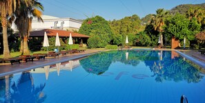 A swimming pool with a clear reflection, surrounded by palm trees and a building with a red roof. - Efe Hotel Göcek (Fethiye)
