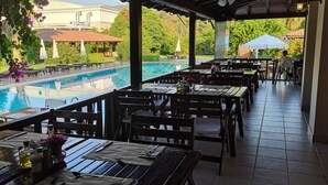 A covered outdoor dining area with tables and chairs, overlooking a swimming pool.