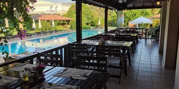 Un espacio exterior techado para comer con mesas y sillas, con vistas a una piscina.