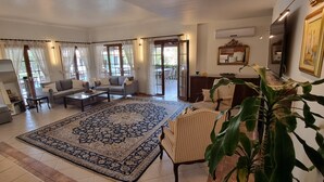 A spacious living room with a large patterned rug, multiple seating options including sofas and chairs, and a dining area with a table and chairs.