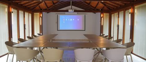 A conference room with a long table and chairs, a projector screen, and wooden beams on the ceiling.