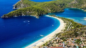 A coastal town with a beach, boats, and lush green hills.