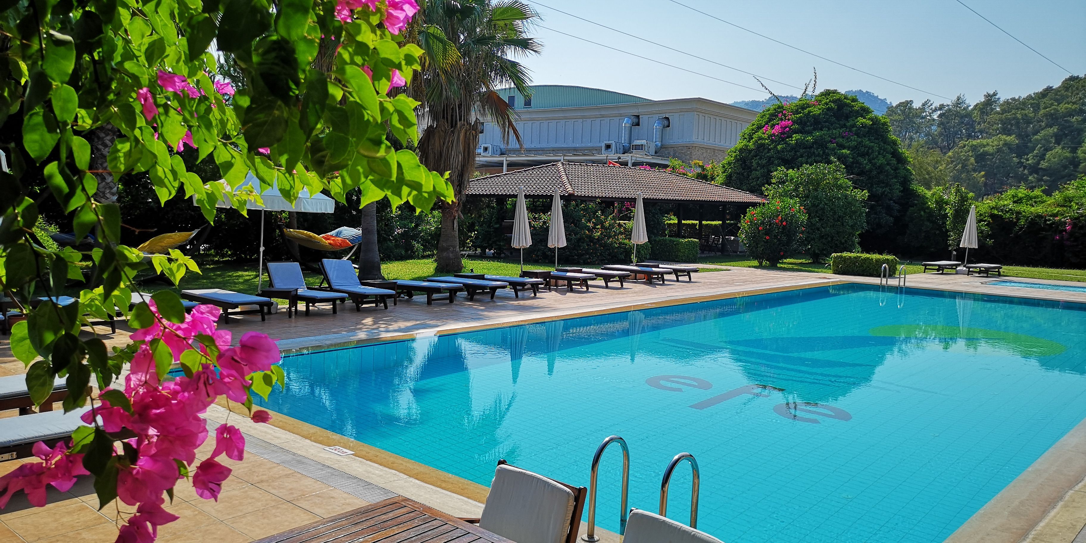 Piscina com espreguiçadeiras e um gazebo em um jardim bem cuidado.