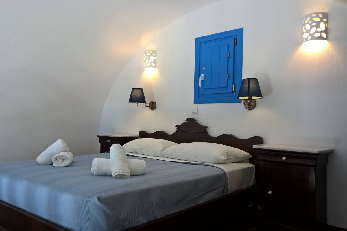 Un lit bien fait, avec des oreillers et des serviettes pliées, une porte bleue et des lampes fixées au mur.