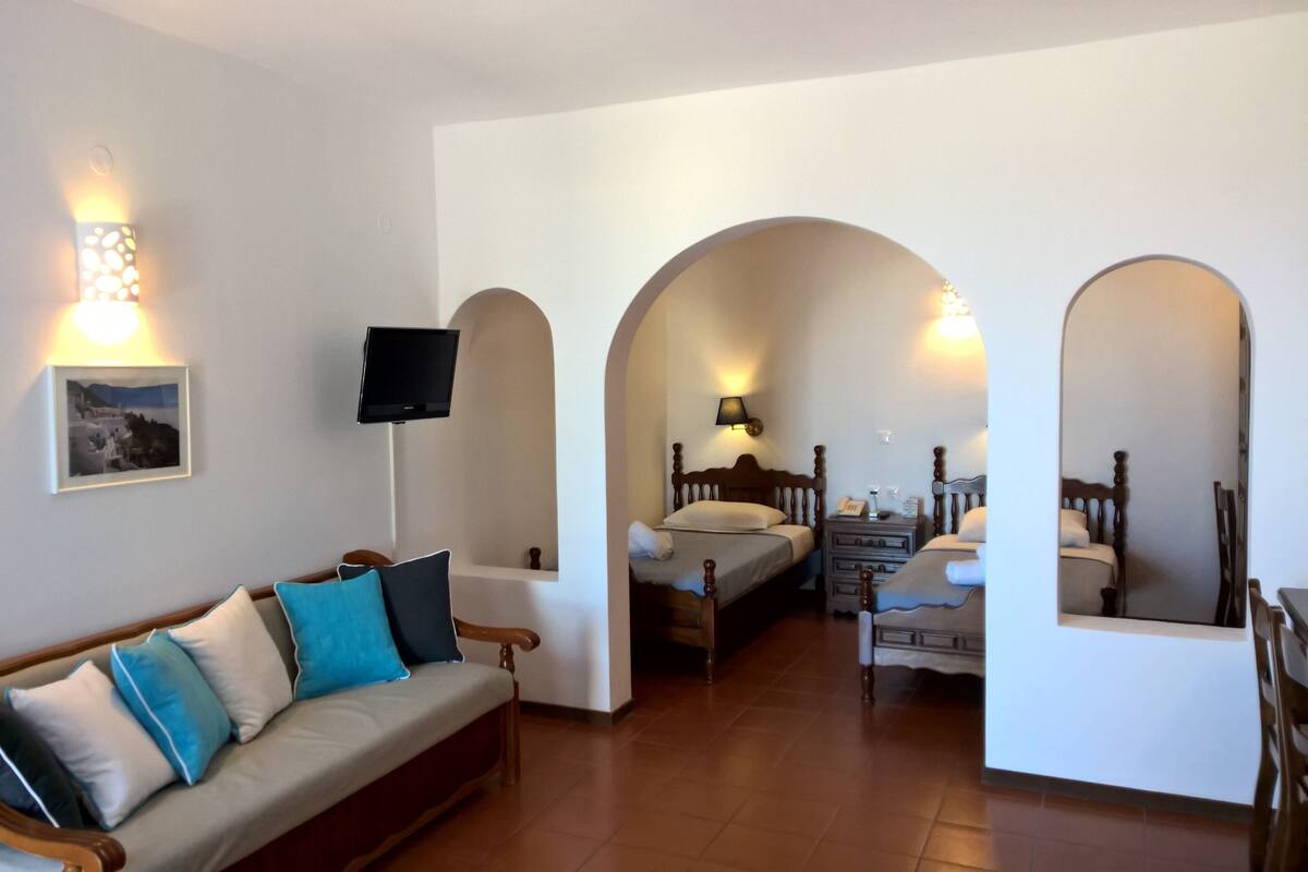 Une chambre d’hôtel avec un canapé, deux lits, une télévision et un tableau au mur.