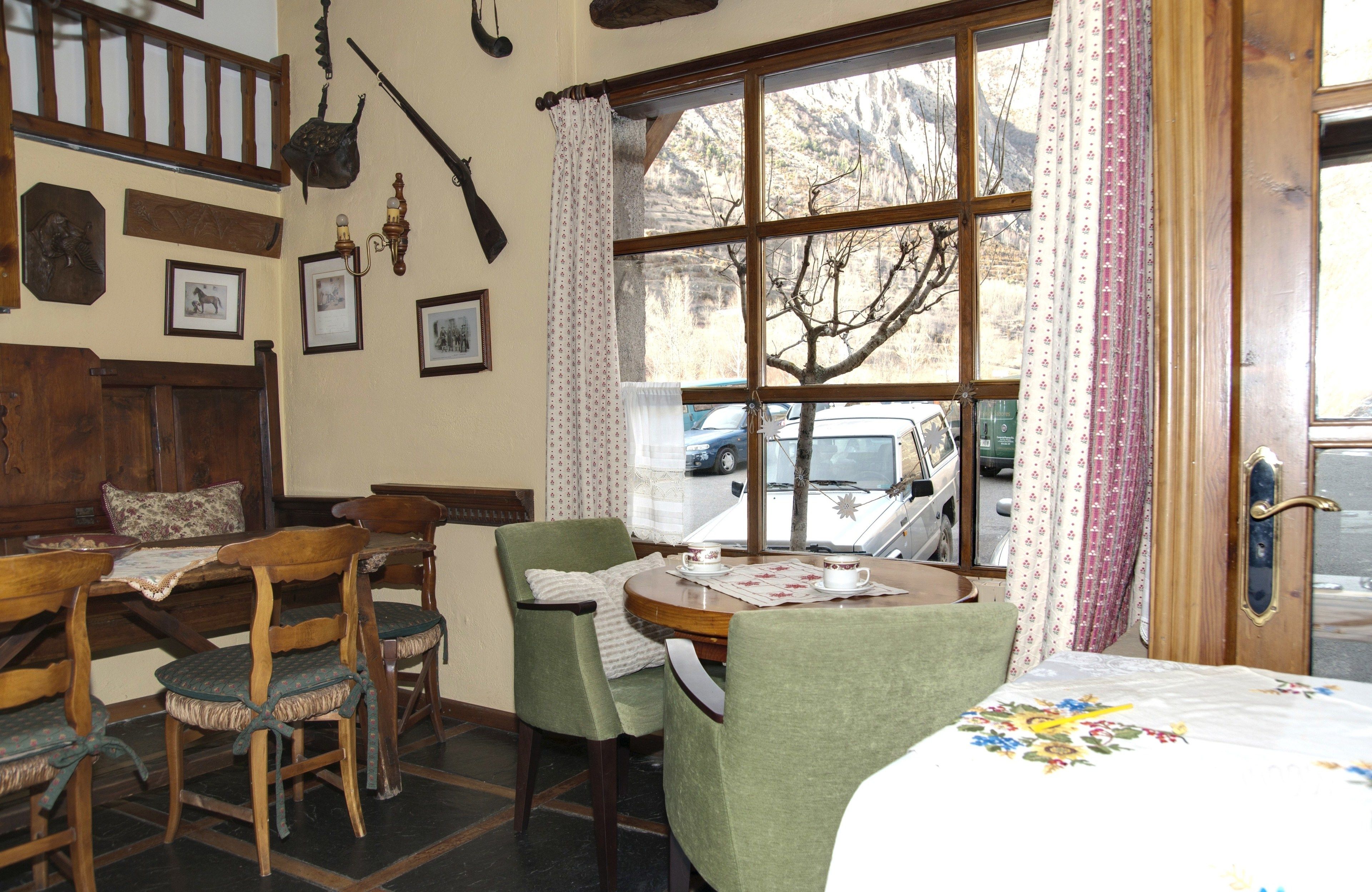 A cozy room with a wooden table, chairs, and a bed. There is a window with curtains and a view of the outside.
