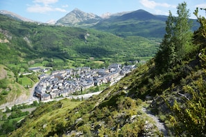 A town nestled in a valley with a mountain backdrop, surrounded by lush greenery and a winding road.