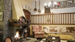A cozy room with a fireplace, a wooden bench, and a floral armchair. - San Marsial Benasque Hotel&Apartamentos (Benasque)