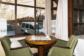 A room with a large window, a round wooden table with two chairs, and a view of a parked van outside.