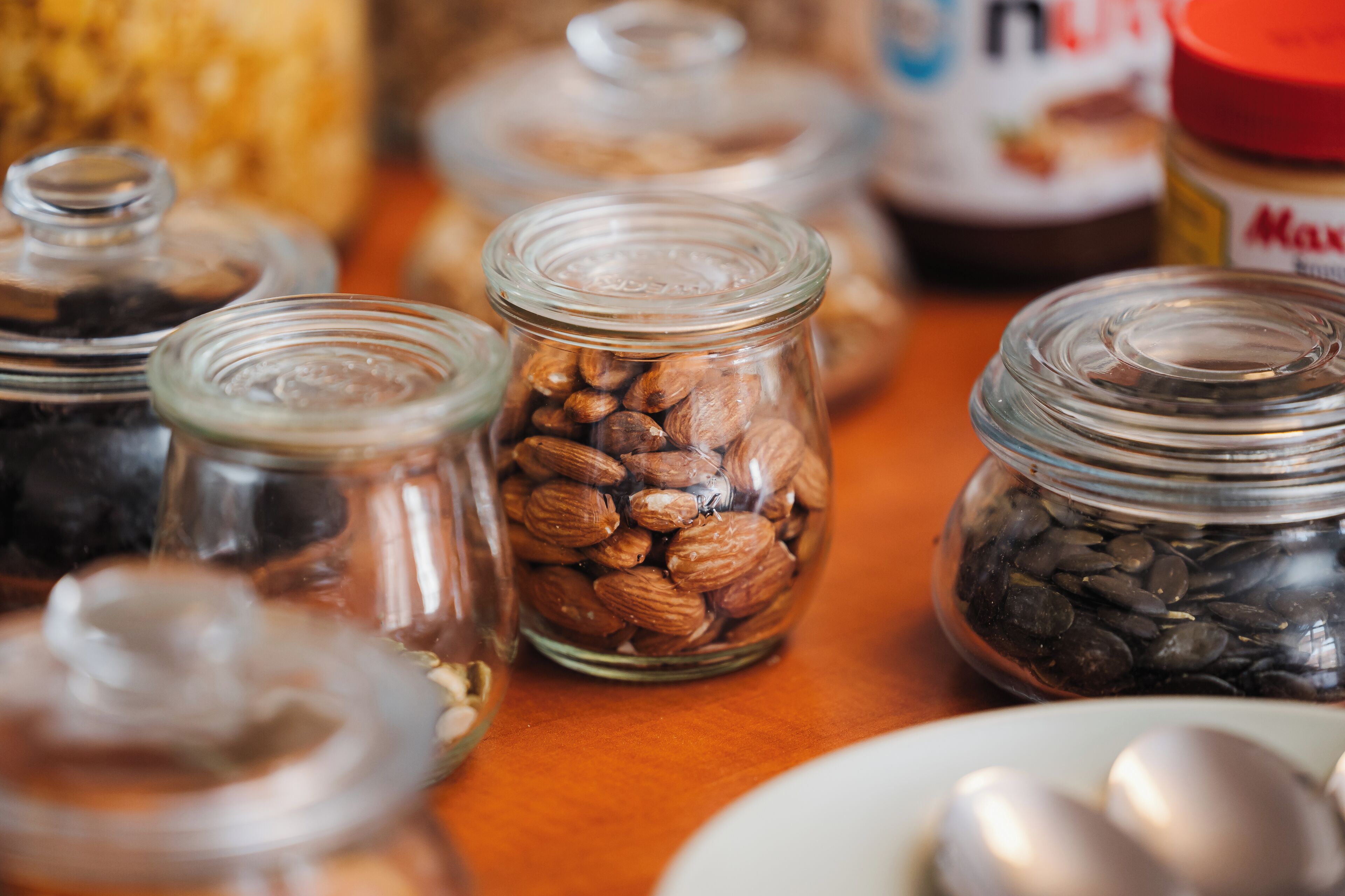 Verschillende glazen potten met diverse soorten noten en zaden op een houten ondergrond.