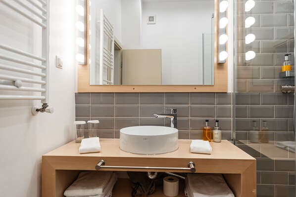 A bathroom with a round sink, a mirror with lights, a towel rack, and a towel dispenser. - Casa Luxemburg (Sibiu)