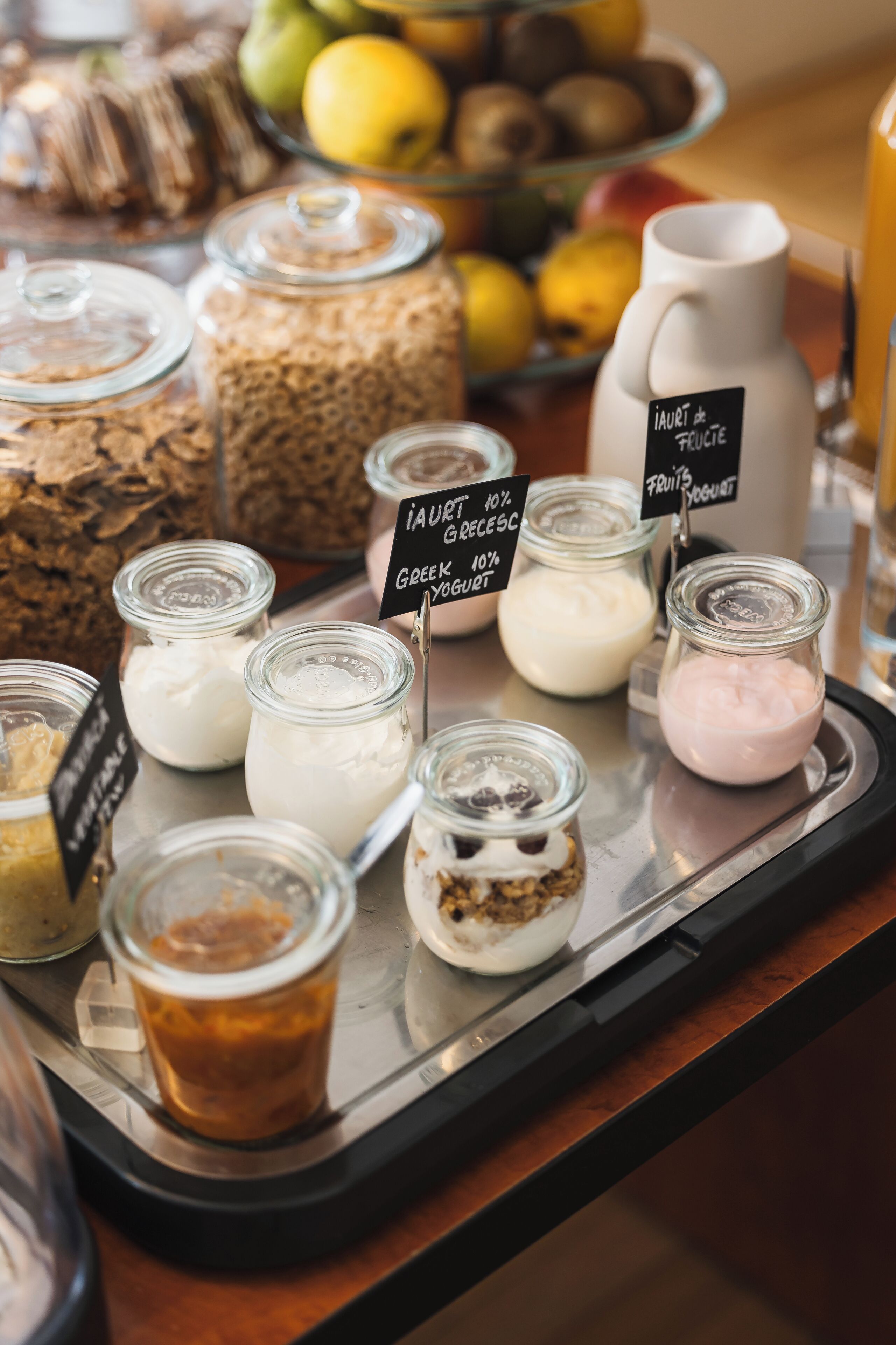 A variety of food items on a tray, including jars of yogurt and other dairy products, with labels indicating flavors like Greek yogurt and fruit yogurt.