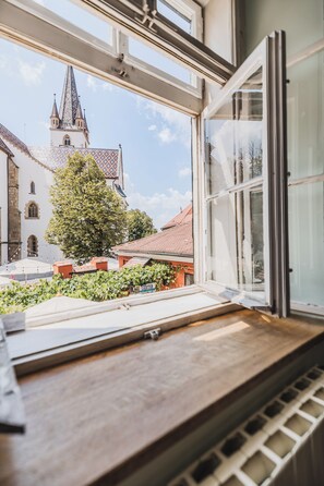 Una habitación con un ventanal grande que da a un patio, una mesa de madera y vistas a una iglesia con una aguja.