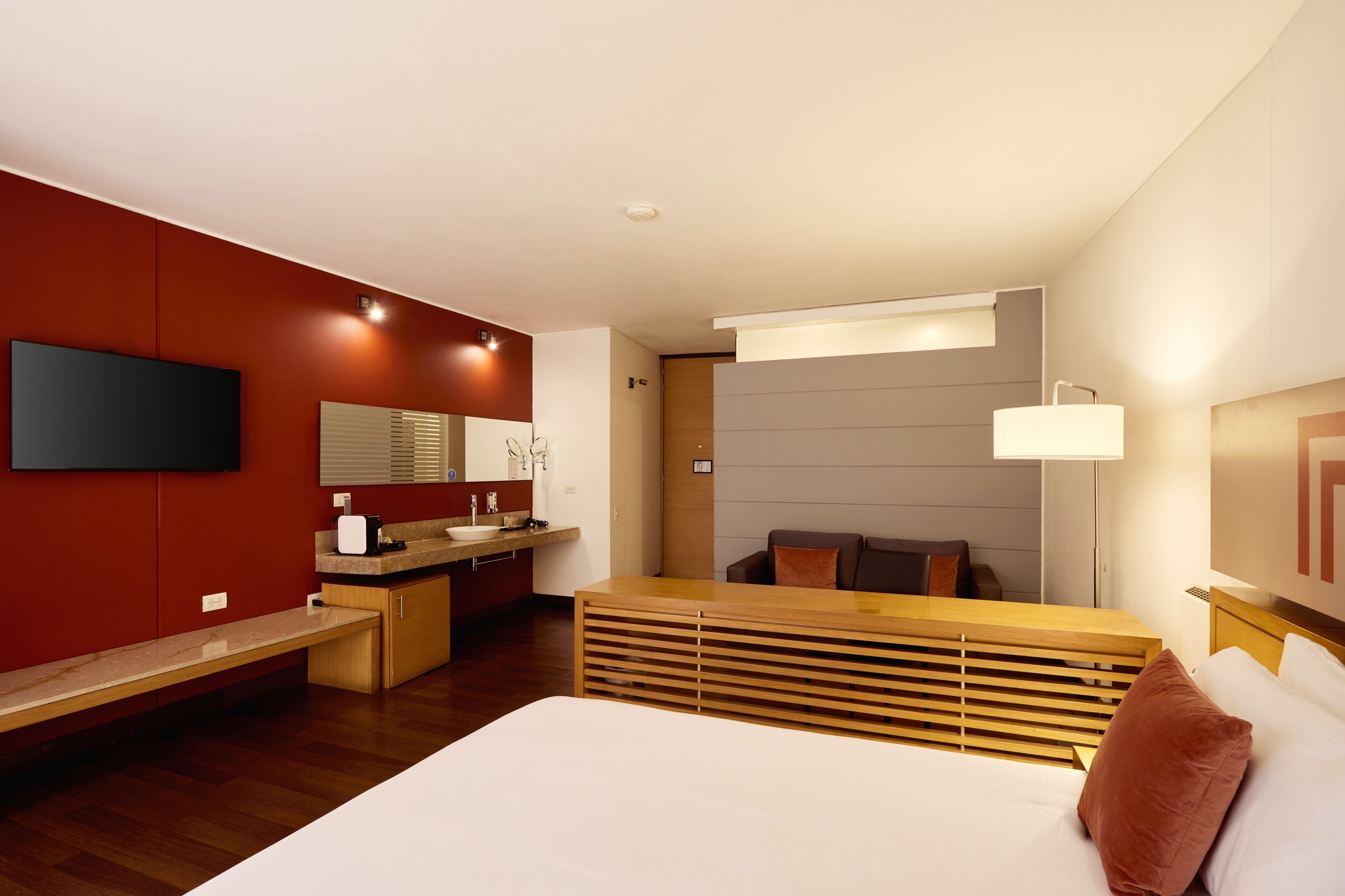 A modern hotel room with a bed, a desk, a television, a bathroom, and a seating area.